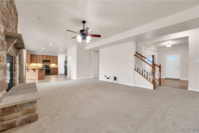 unfurnished living room featuring ceiling fan, carpet flooring, and a stone fireplace