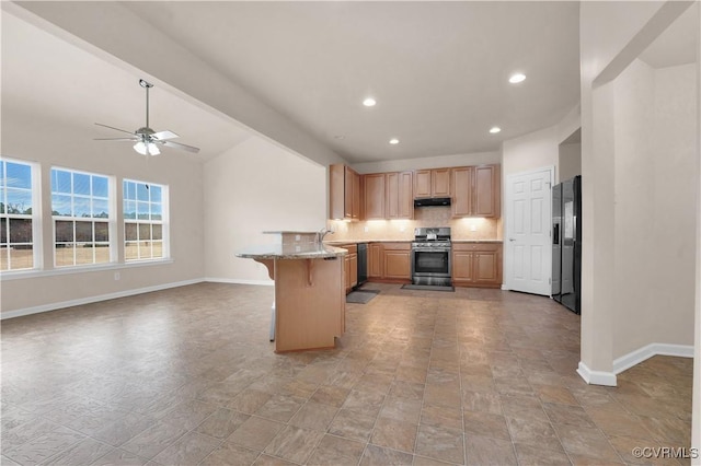 kitchen featuring a kitchen bar, kitchen peninsula, ceiling fan, appliances with stainless steel finishes, and light stone countertops