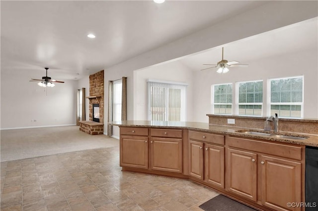 kitchen featuring light carpet, a stone fireplace, ceiling fan, sink, and light stone counters