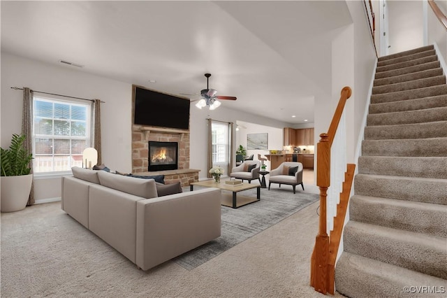 carpeted living room with ceiling fan, plenty of natural light, and a stone fireplace