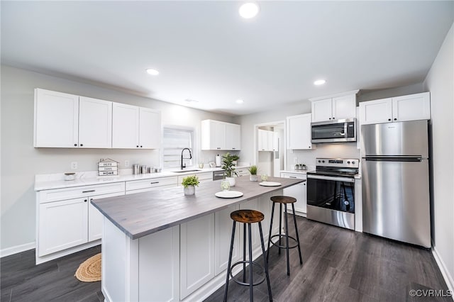 kitchen featuring appliances with stainless steel finishes, sink, dark wood-type flooring, white cabinets, and a center island