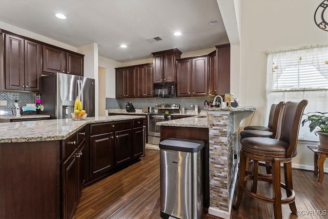 kitchen with appliances with stainless steel finishes, dark hardwood / wood-style floors, backsplash, a kitchen breakfast bar, and kitchen peninsula