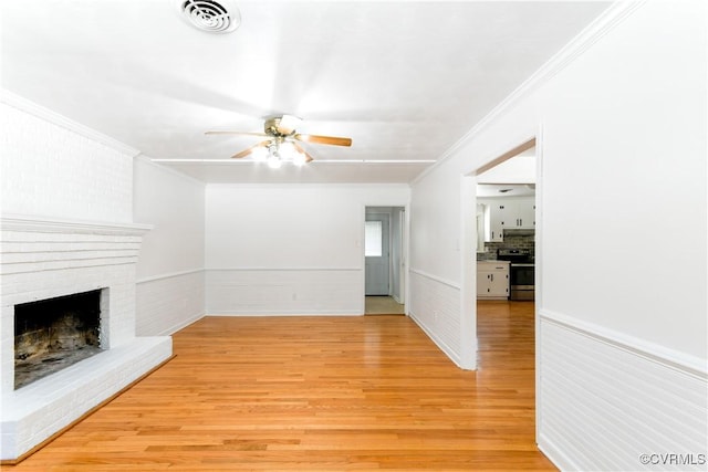 unfurnished living room featuring light wood-type flooring, a brick fireplace, ornamental molding, and ceiling fan