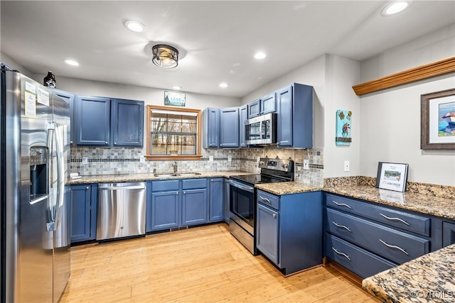 kitchen with blue cabinetry, sink, light wood-type flooring, stainless steel appliances, and backsplash