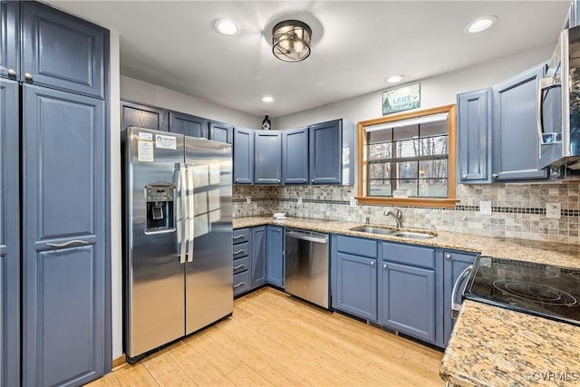 kitchen with appliances with stainless steel finishes, blue cabinets, sink, and light stone countertops