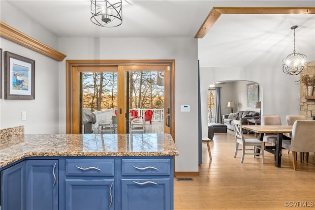 kitchen featuring blue cabinetry, an inviting chandelier, light wood-type flooring, pendant lighting, and light stone countertops