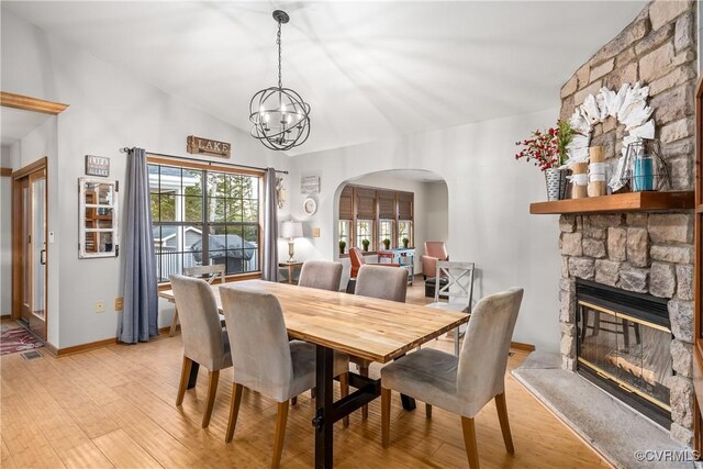 dining room featuring a stone fireplace, lofted ceiling, a chandelier, and light hardwood / wood-style flooring