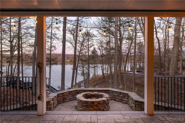 patio terrace at dusk featuring a water view and an outdoor fire pit