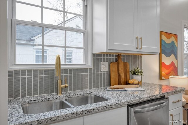 kitchen with light stone countertops, white cabinets, tasteful backsplash, sink, and stainless steel dishwasher