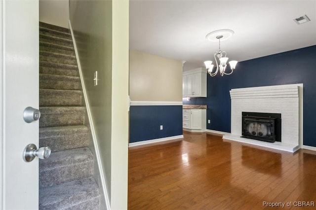 unfurnished living room with a brick fireplace, dark hardwood / wood-style flooring, and an inviting chandelier