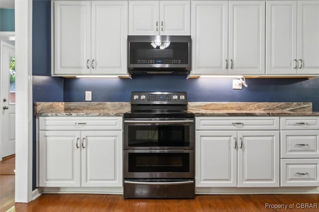 kitchen featuring light hardwood / wood-style flooring, dark stone countertops, stainless steel appliances, and white cabinetry