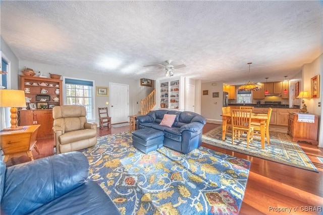 living room with hardwood / wood-style flooring, ceiling fan, built in shelves, and a textured ceiling