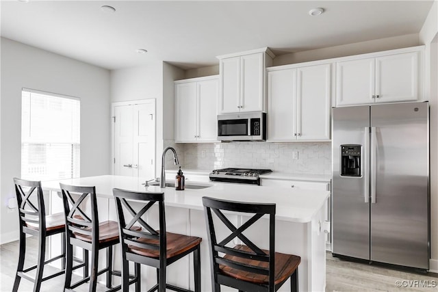 kitchen featuring white cabinetry, sink, light wood-type flooring, stainless steel appliances, and a center island with sink