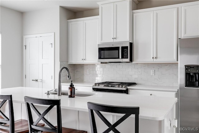 kitchen with sink, white cabinetry, stainless steel appliances, and a breakfast bar area