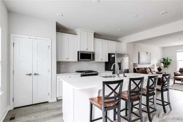 kitchen with appliances with stainless steel finishes, white cabinetry, decorative backsplash, a center island with sink, and a breakfast bar area