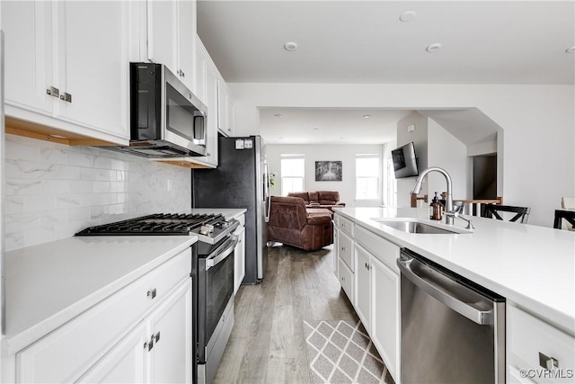 kitchen with appliances with stainless steel finishes, white cabinetry, decorative backsplash, sink, and light wood-type flooring