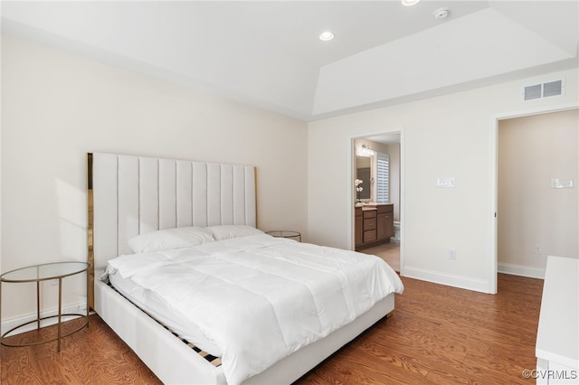 bedroom featuring wood-type flooring, a tray ceiling, and ensuite bath