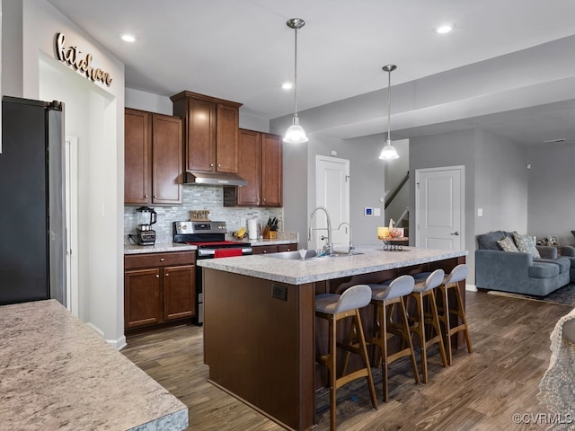 kitchen with sink, hanging light fixtures, a center island with sink, appliances with stainless steel finishes, and dark hardwood / wood-style floors