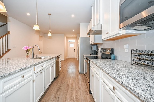 kitchen with pendant lighting, appliances with stainless steel finishes, sink, white cabinets, and light stone counters