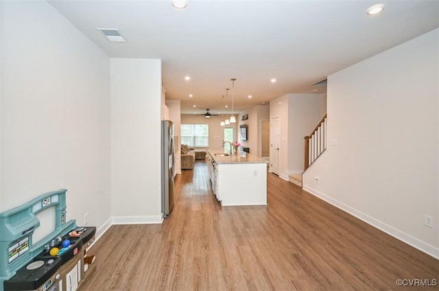 kitchen with decorative light fixtures, a center island with sink, sink, and white cabinetry