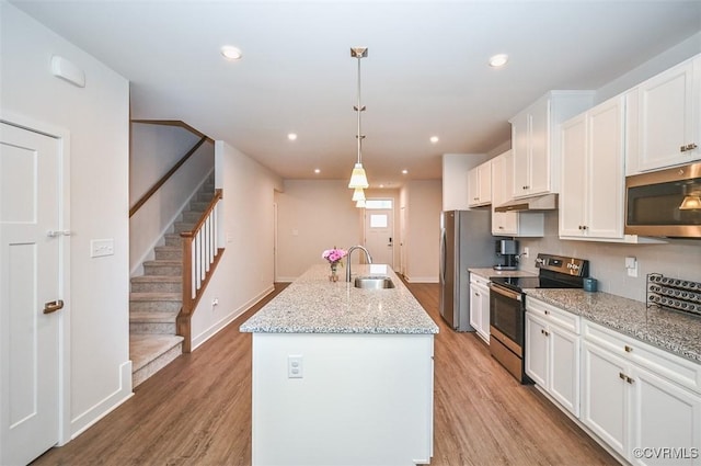 kitchen featuring pendant lighting, white cabinetry, stainless steel appliances, and an island with sink