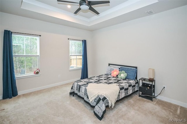 carpeted bedroom with ceiling fan, multiple windows, and a tray ceiling