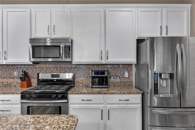 kitchen with stainless steel appliances, dark stone counters, and white cabinets