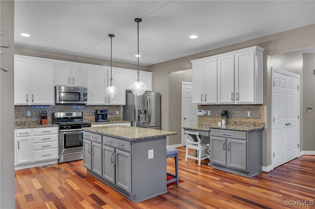 kitchen with appliances with stainless steel finishes, white cabinetry, hanging light fixtures, a kitchen island, and a kitchen bar