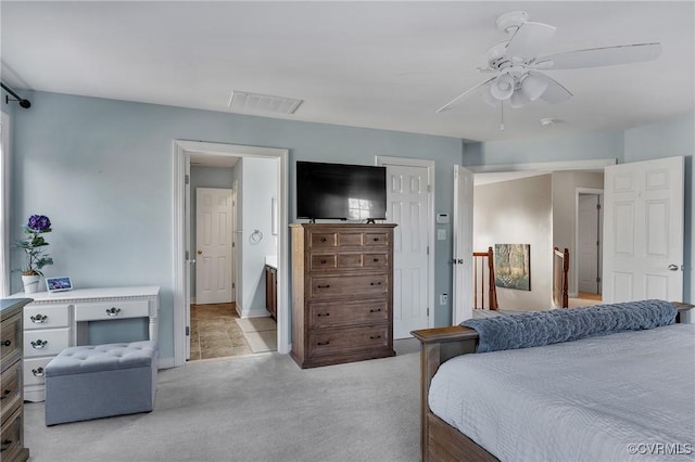 bedroom with ceiling fan, light colored carpet, and ensuite bath