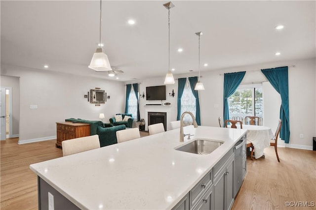 kitchen featuring light hardwood / wood-style floors, gray cabinetry, sink, pendant lighting, and an island with sink