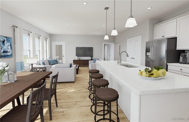 kitchen with white cabinets, sink, pendant lighting, an island with sink, and stainless steel fridge