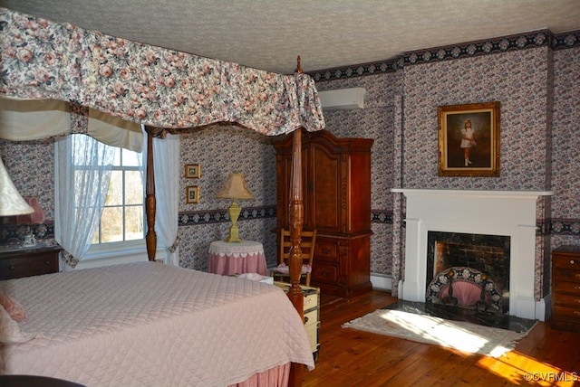 bedroom with an AC wall unit, wood-type flooring, and a textured ceiling