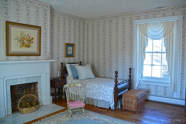 bedroom featuring wood-type flooring, baseboard heating, a textured ceiling, and a premium fireplace