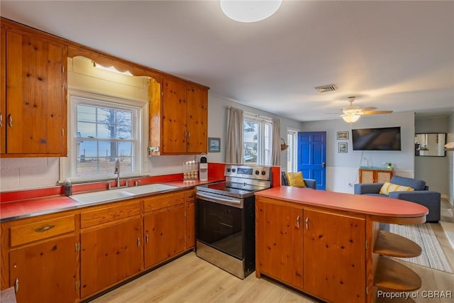 kitchen with kitchen peninsula, ceiling fan, sink, stainless steel range with electric cooktop, and light hardwood / wood-style floors