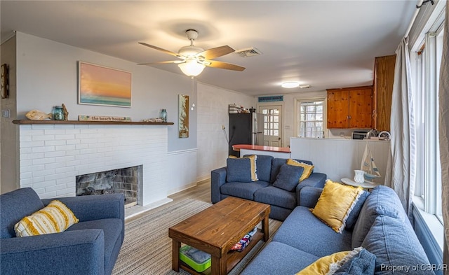 living room featuring ceiling fan, light hardwood / wood-style flooring, and a fireplace