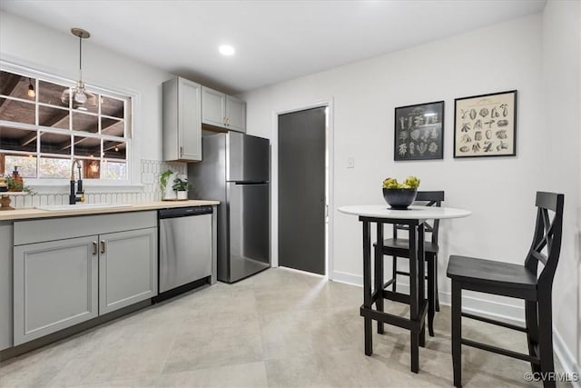 kitchen featuring gray cabinets, pendant lighting, sink, backsplash, and stainless steel appliances