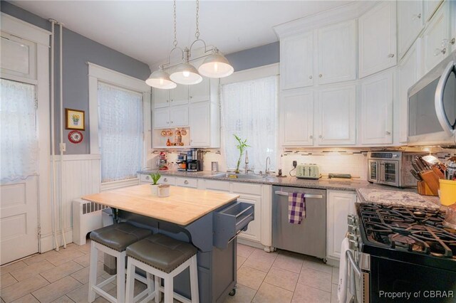 kitchen with appliances with stainless steel finishes, a kitchen island, white cabinetry, tasteful backsplash, and a kitchen breakfast bar