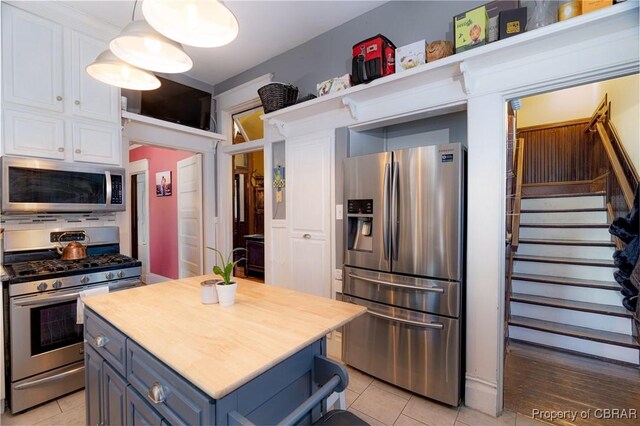 kitchen with blue cabinetry, light tile patterned floors, white cabinets, decorative light fixtures, and stainless steel appliances