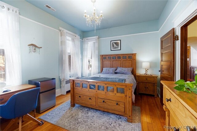 bedroom featuring light wood-type flooring, stainless steel fridge, and a notable chandelier