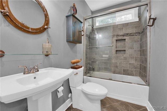 bathroom featuring toilet, tile patterned flooring, bath / shower combo with glass door, and a sink