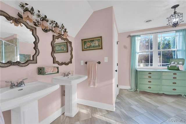 bathroom with visible vents, two sinks, vaulted ceiling, a shower stall, and baseboards