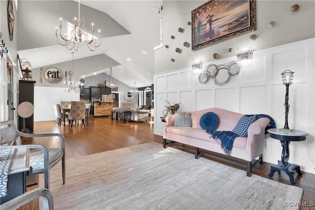 living room featuring high vaulted ceiling, an inviting chandelier, wood finished floors, and a decorative wall