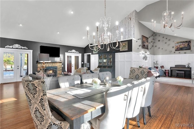 dining space featuring french doors, wainscoting, wood finished floors, a stone fireplace, and a chandelier