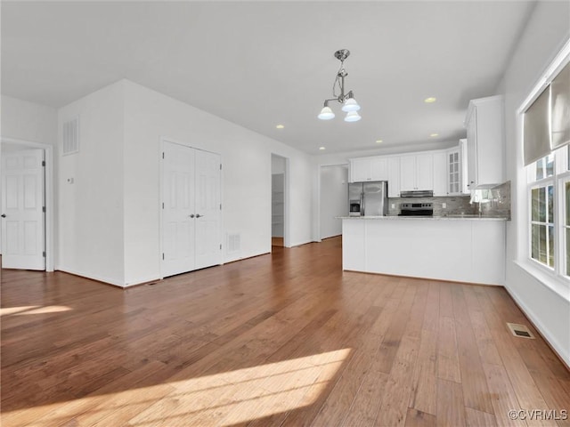 kitchen featuring white cabinets, appliances with stainless steel finishes, wood-type flooring, tasteful backsplash, and kitchen peninsula