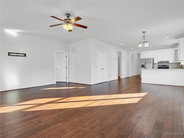 unfurnished living room featuring ceiling fan with notable chandelier and dark wood-type flooring