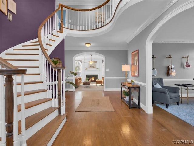 entrance foyer featuring arched walkways, a warm lit fireplace, wood finished floors, and crown molding