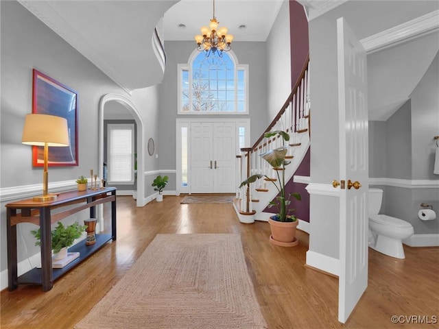 foyer entrance featuring a notable chandelier, a towering ceiling, hardwood / wood-style floors, and crown molding