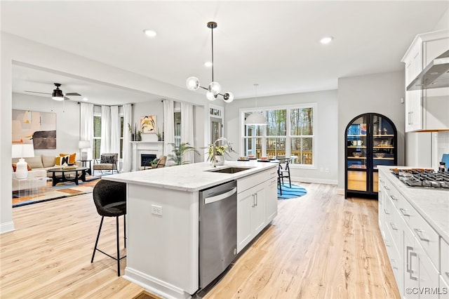 kitchen with sink, appliances with stainless steel finishes, a kitchen island with sink, light stone counters, and white cabinets