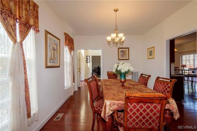 dining room with dark wood-type flooring, a wealth of natural light, and an inviting chandelier