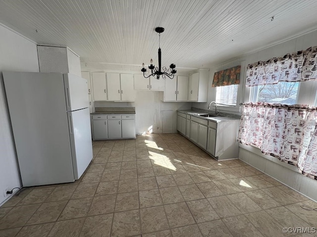 kitchen featuring hanging light fixtures, sink, white refrigerator, white cabinetry, and a notable chandelier